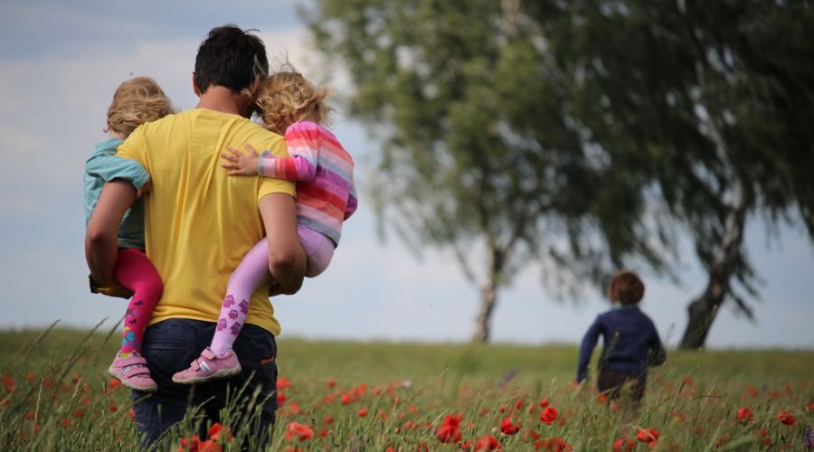 man holding two children in a field