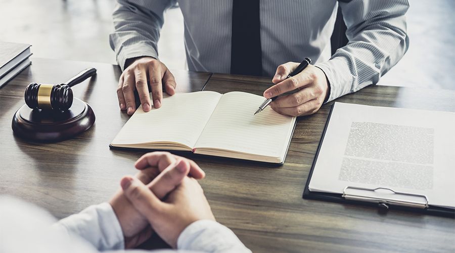 man writing in ledger in front of another man at a desk